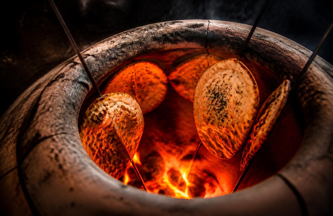 Naan baking against the glowing coals of a clay tandoor oven